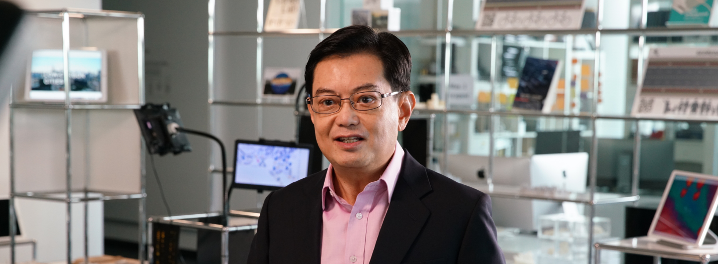 Man in glasses, pink shirt and suit, facing forward, in an office-like setting.